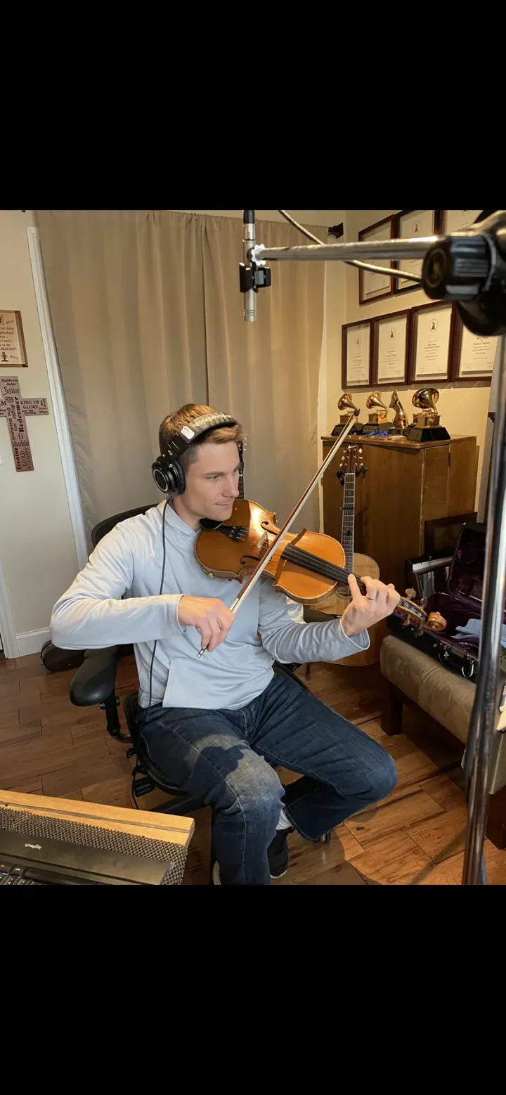 Andy Leftwich playing fiddle while seated in the studio.