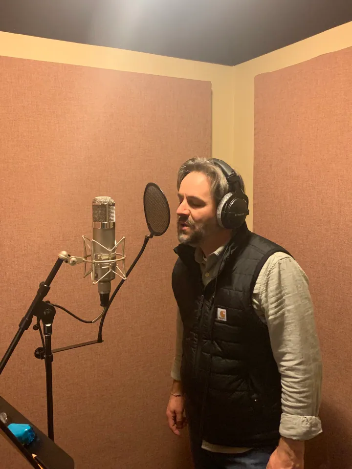 Jeremy Casella wearing headphones at a vocal microphone.