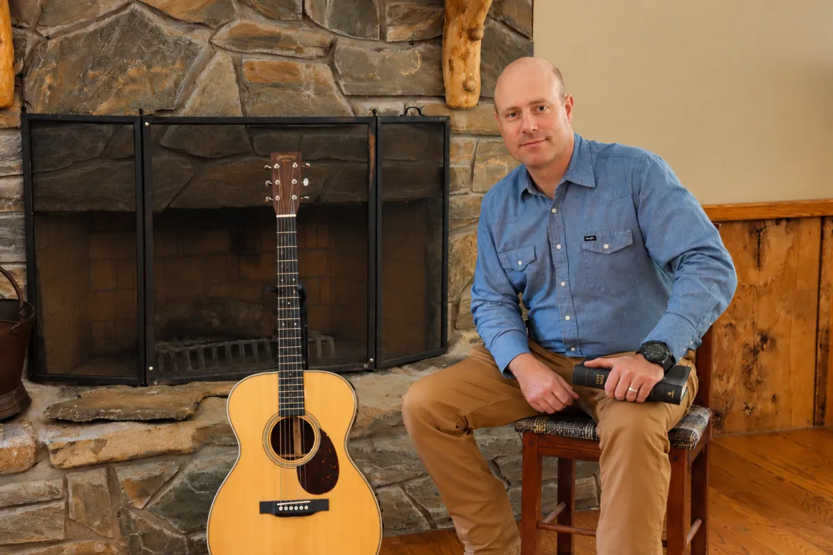 Sam with his guitar and Bible beside a stone fireplace